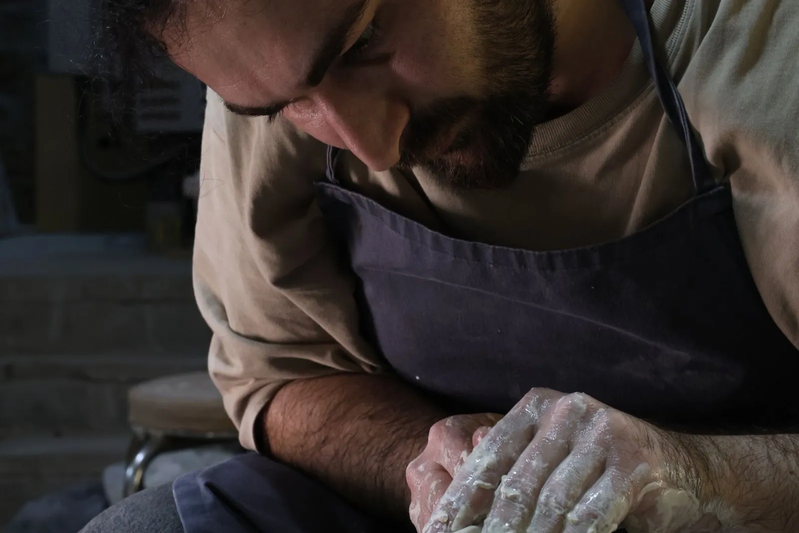 A potter's clay-covered hands shape a small vessel on a spinning pottery wheel.