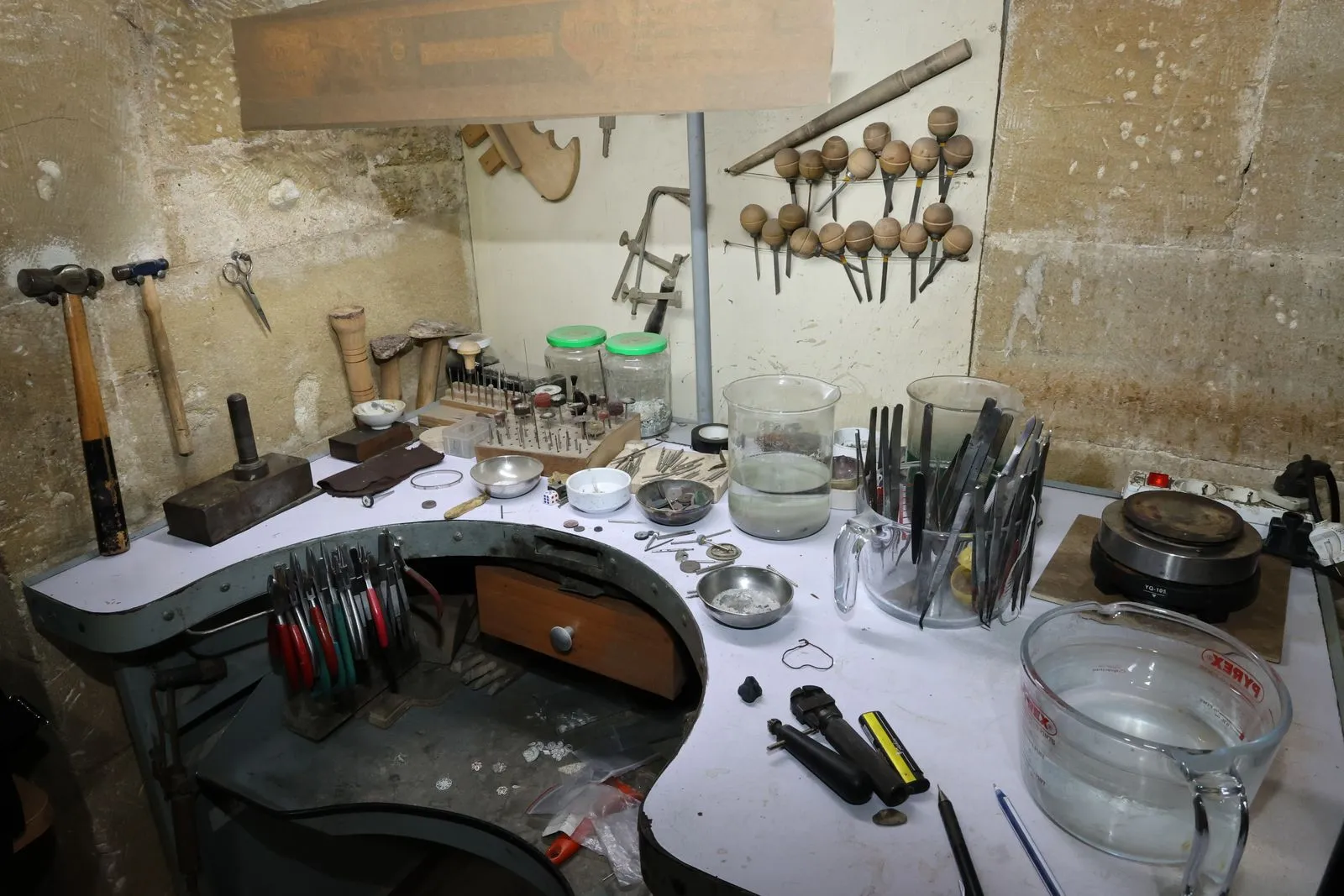 A jewelry maker's workbench covered in hand tools, tweezers, and small metal components.