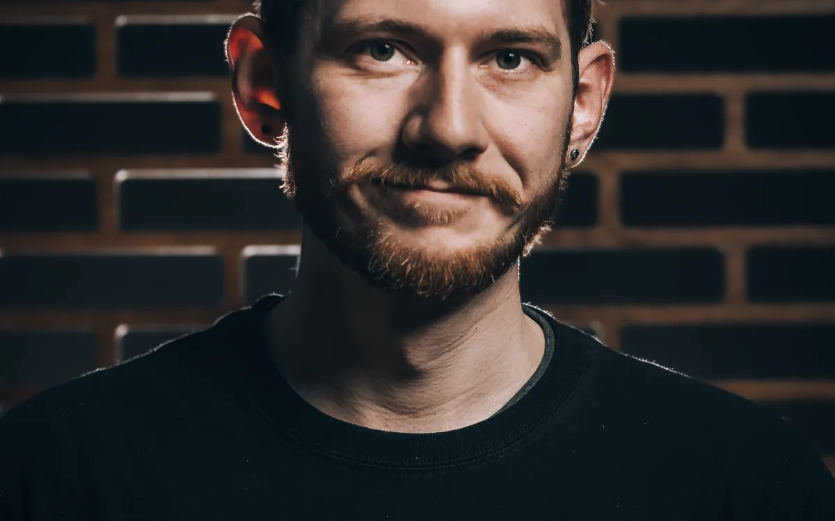 Ben Spear — portrait, wearing a backward cap, photographed against the studio's brick-accent wall.